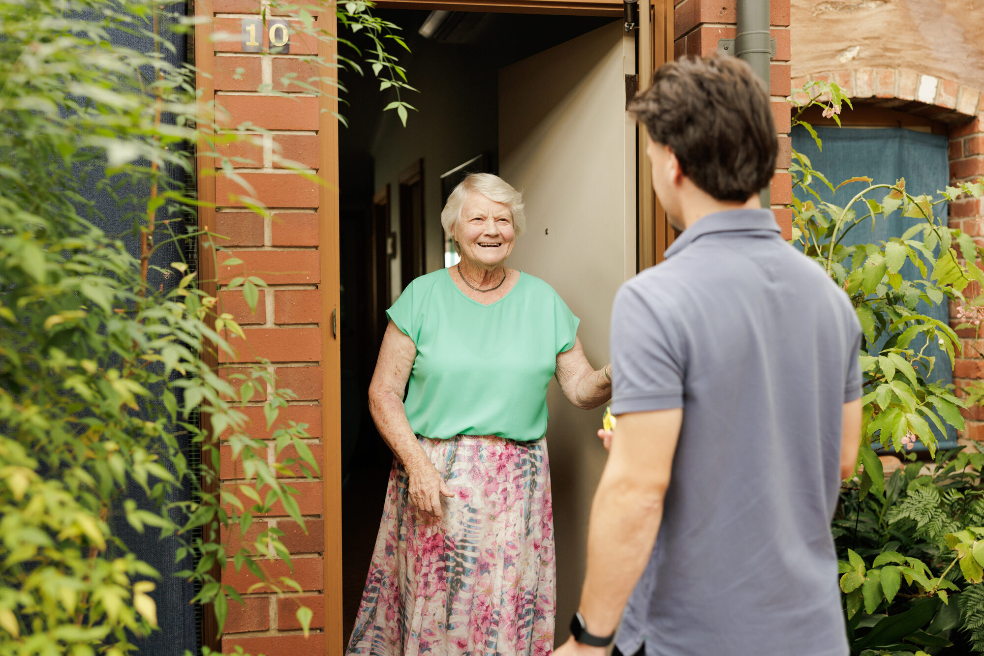 A resident welcoming a visitor at her front door.